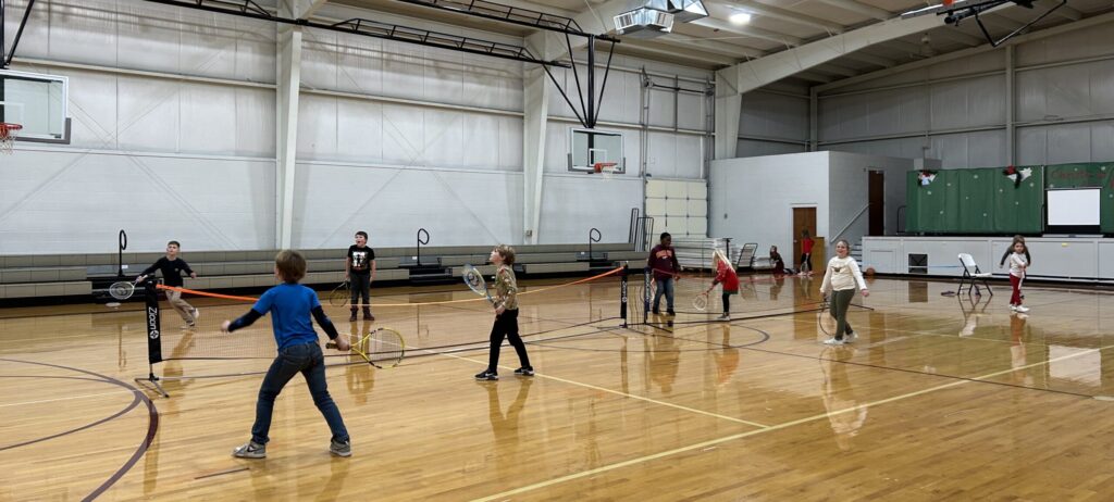 a group of kids learning tennis together in a school gym participating in a tennis program taught by a SATA coach