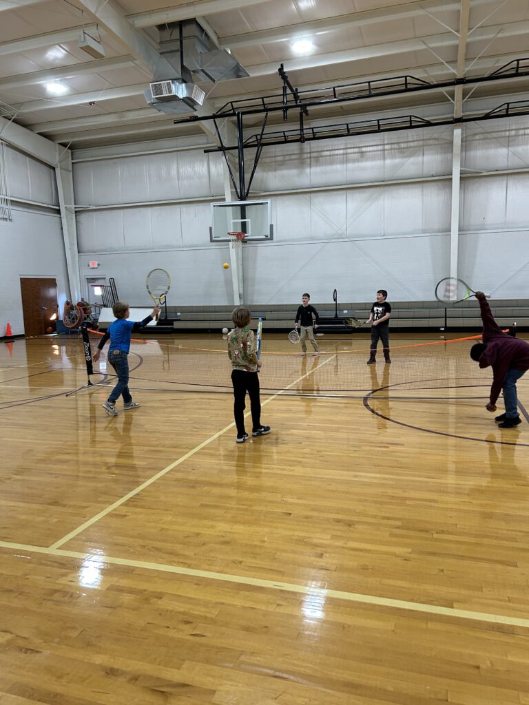 a group of kids learning tennis together in a school gym participating in a tennis program